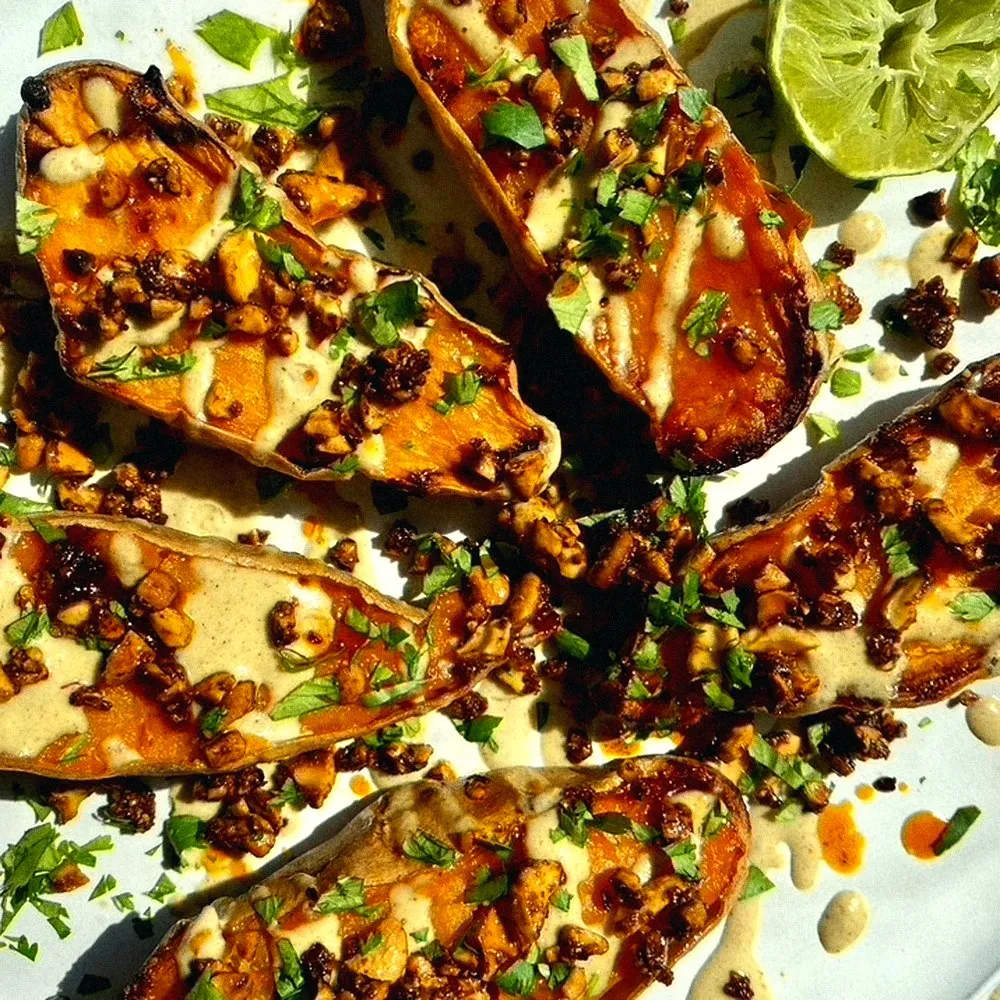 Roasted sweet potato halves with tahini, chili crisp and cilantro, limes alongside