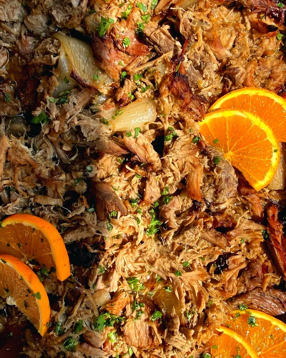 A tray of slow-roasted pulled pork with orange slices and chopped herbs