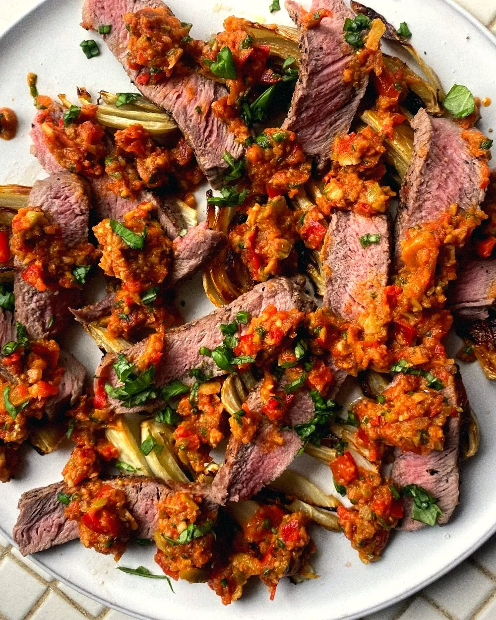 Sliced steak with roasted fennel and a chopped pepper salsa on a white plate