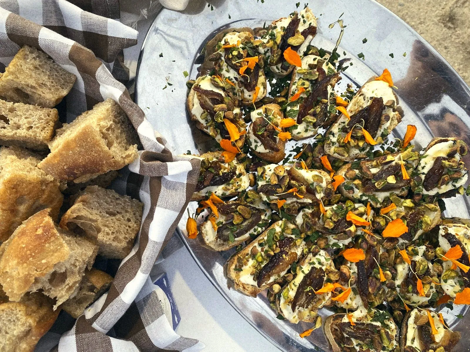 Torn bread in a gingham-lined basket beside a platter of ricotta crostini
