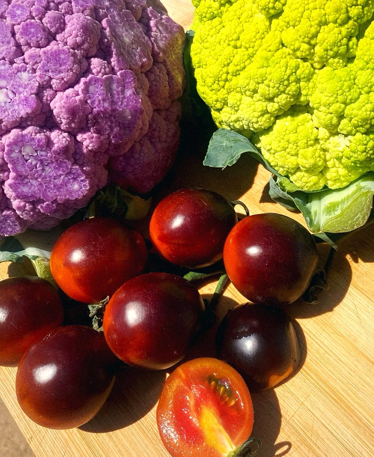 Purple and green cauliflower with dark heirloom tomatoes on a cutting board