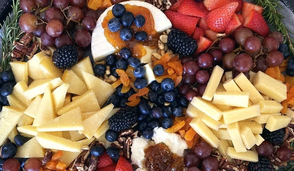 A cheese board with grapes, berries, dried apricots, pecans and brie