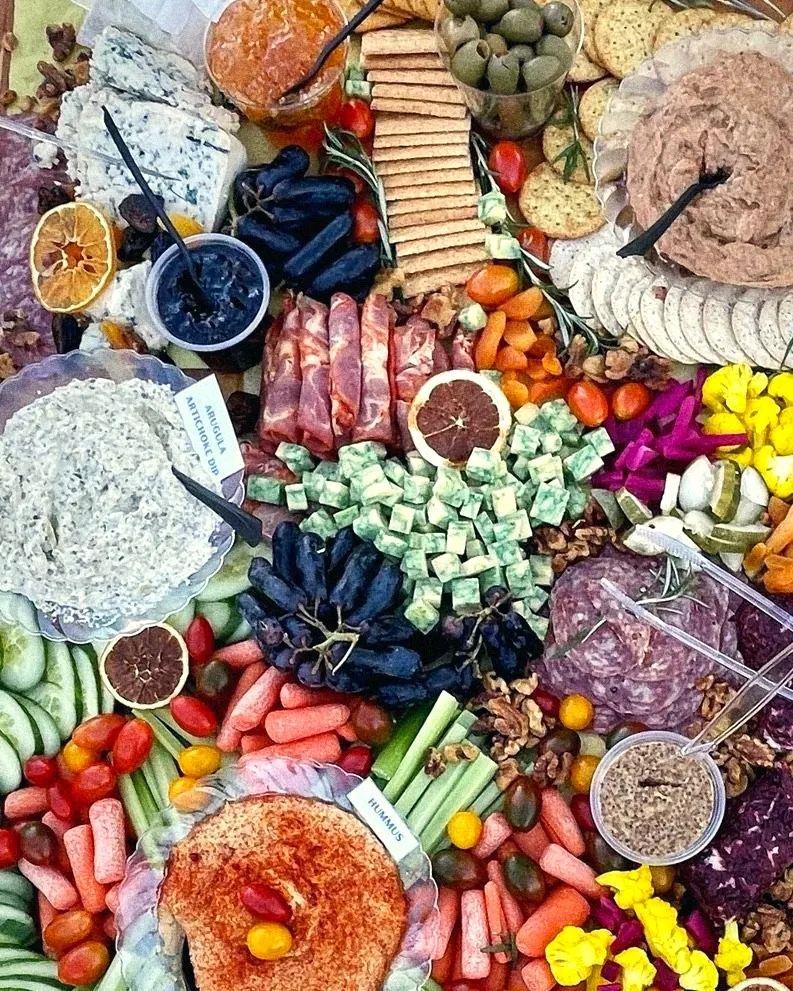 A grazing board close up: blue cheese, salami, crackers, dips and pickled cauliflower
