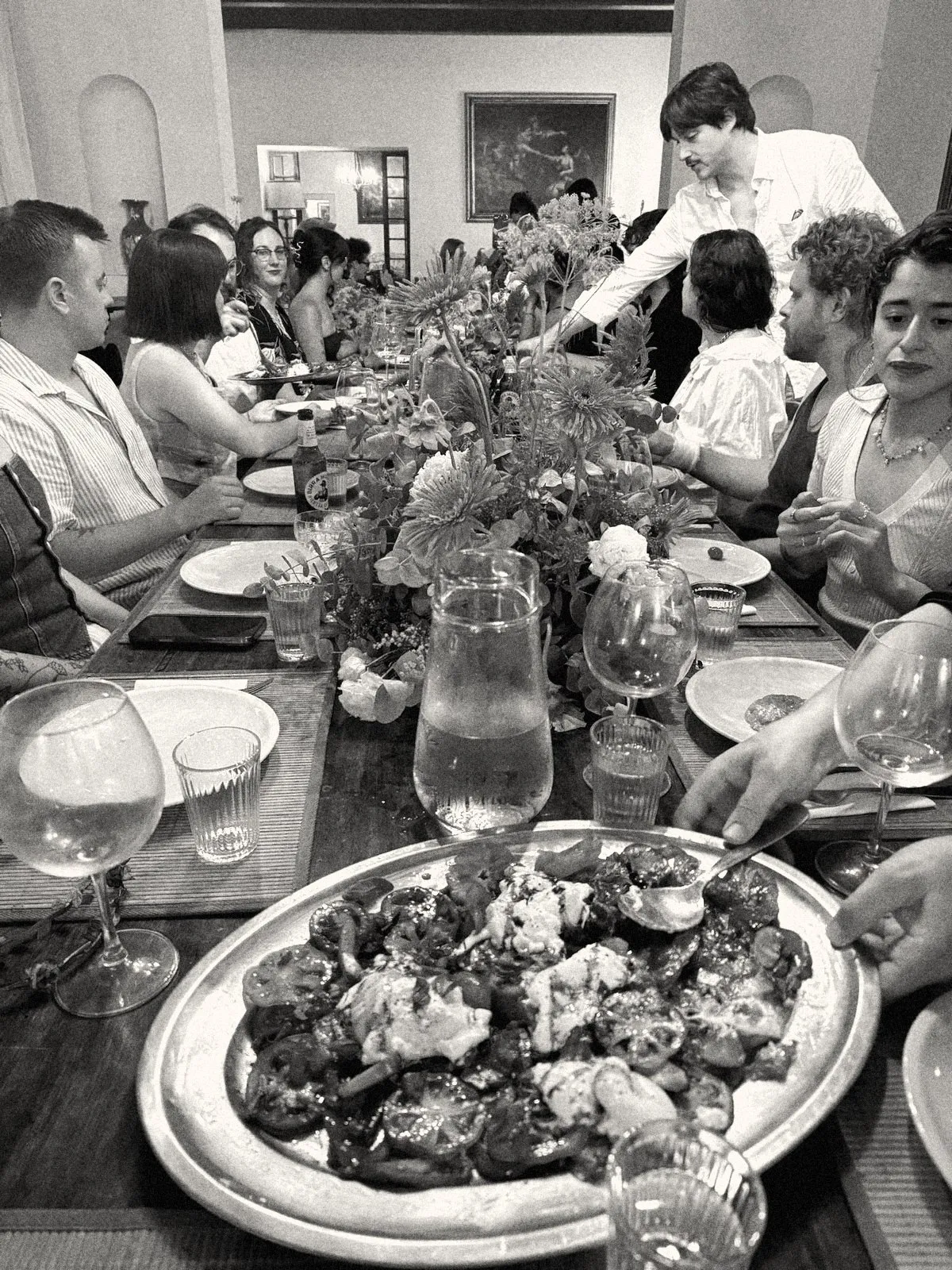 A long dinner table with orange gerberas and a platter of heirloom tomatoes and burrata