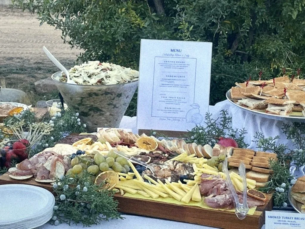 An outdoor buffet with a printed menu, grazing board and finger sandwiches