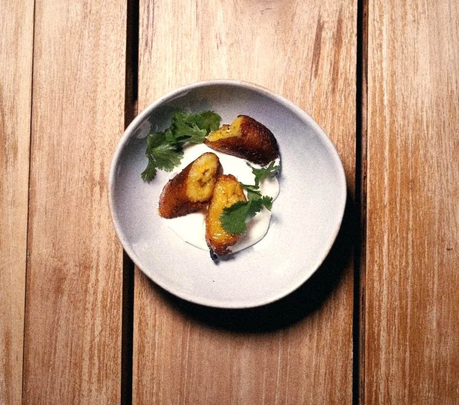 Fried plantains over crema with cilantro in a stoneware bowl