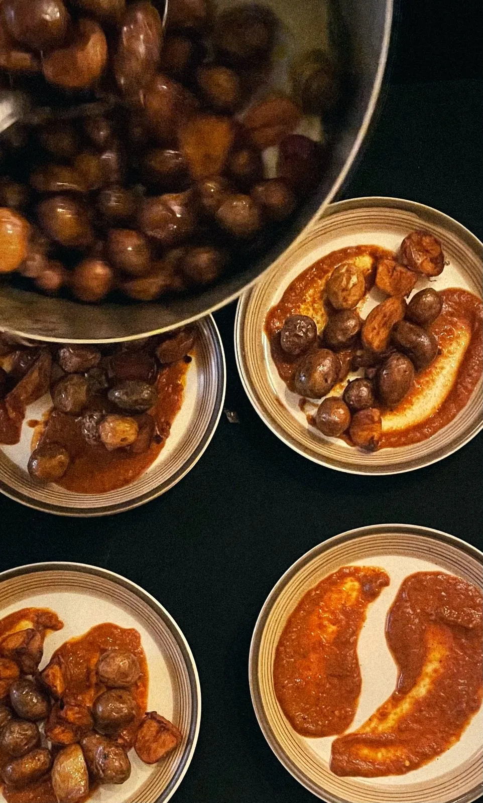 Roasted baby potatoes being plated over romesco