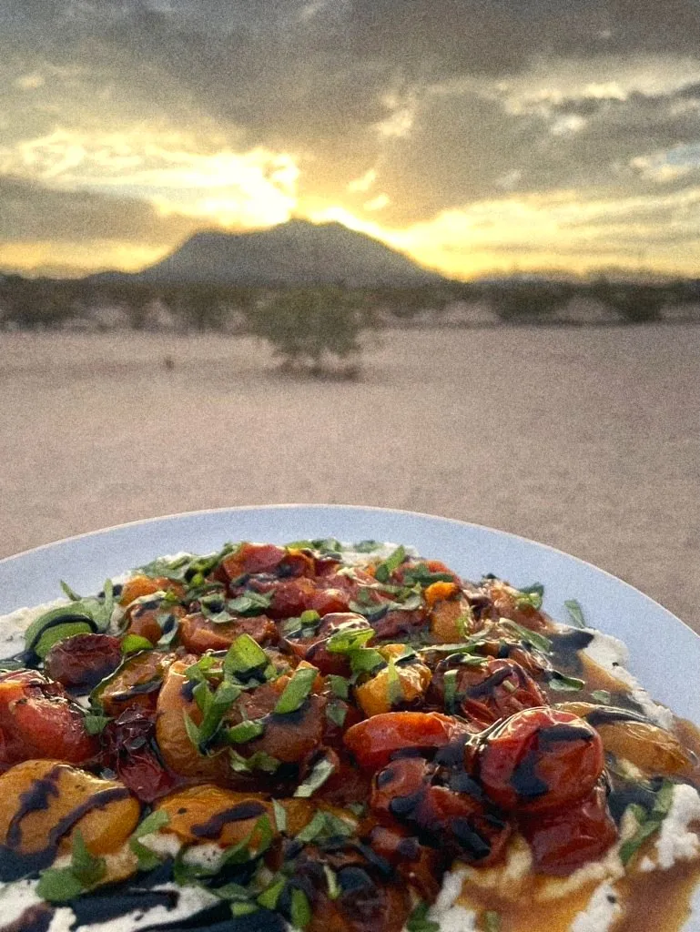 Blistered tomatoes over ricotta with the desert sunset behind