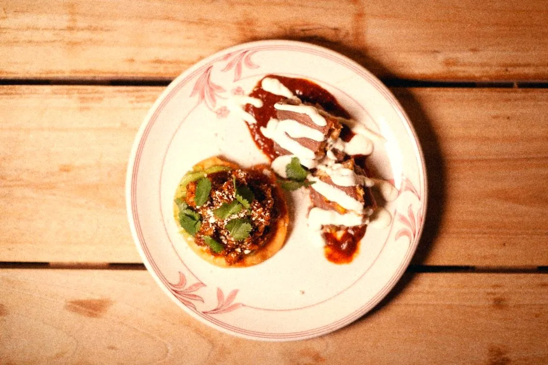A tostada and enchilada with crema on a vintage plate