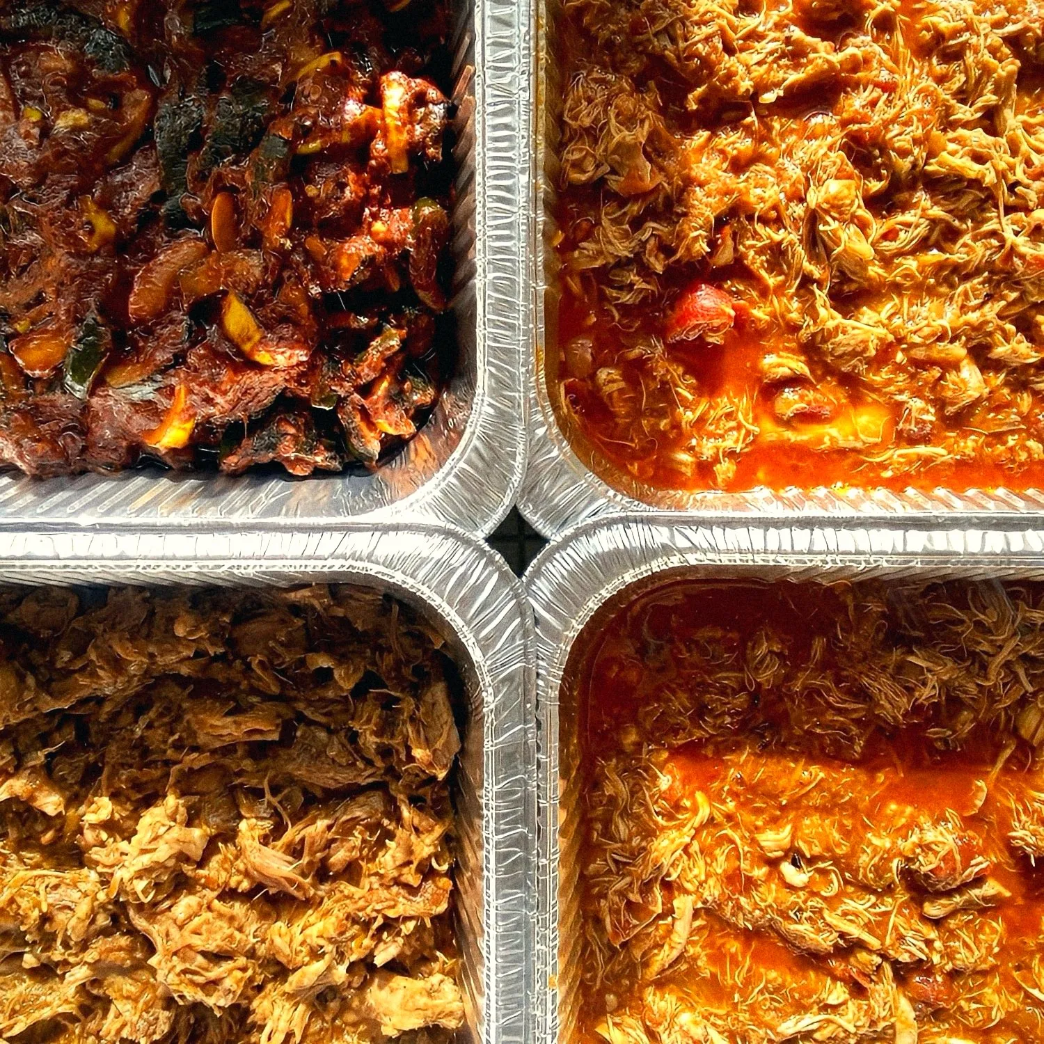 Four trays of braised meats and roasted vegetables ready for delivery