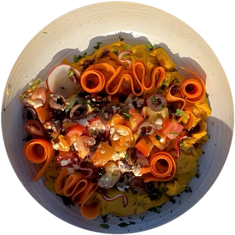 Turmeric hummus with shaved carrot, olives and tomato in a speckled bowl