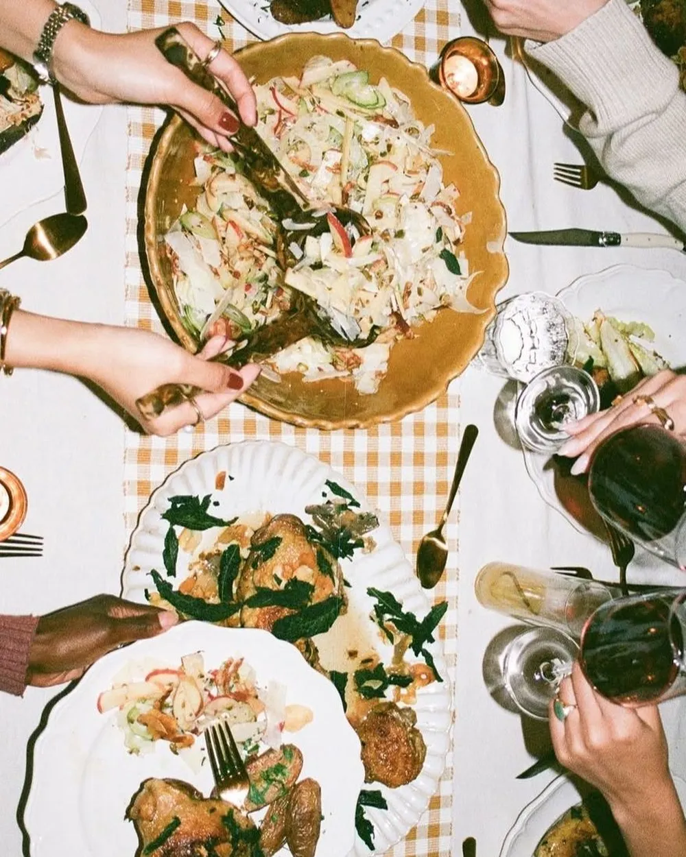 Friends reaching across a long table for a fennel and apple salad, roasted chicken and potatoes